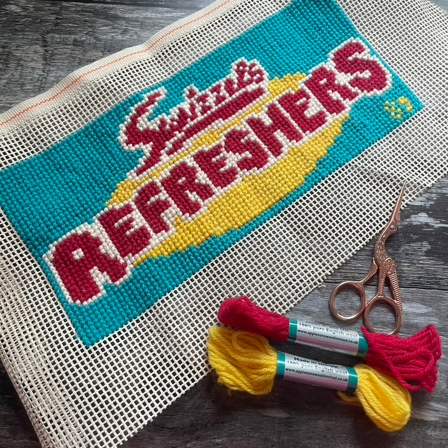 Cross-stitched design of Refreshers picknmix with embroidery threads and scissors on a wooden surface. Copyright Jacqui Pearce