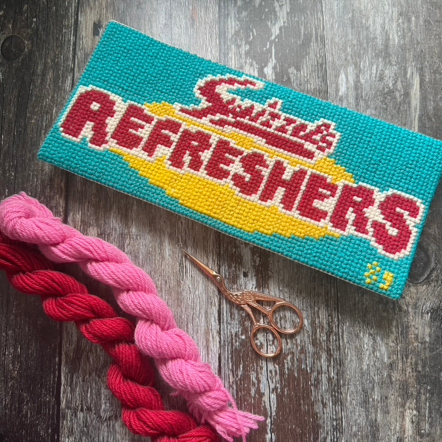 Cross-stitched Refreshers with braided yarn and scissors on a wooden surface copyright jacqui pearce