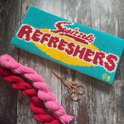 Cross-stitched Refreshers with braided yarn and scissors on a wooden surface copyright jacqui pearce