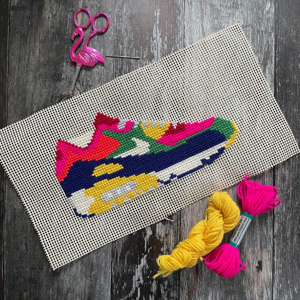 Cross-stitching project with colorful shoe design on a wooden surface with yarn and scissors.