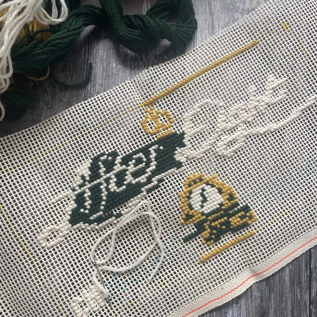 After Eight Tuck Shop Cross-stitched design on fabric with threads and a wooden needle on a wooden surface