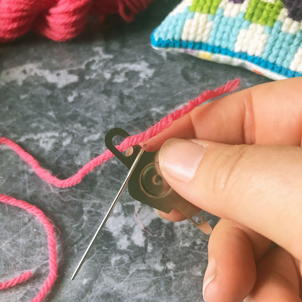 Hand threading a needle with pink yarn on a textured surface