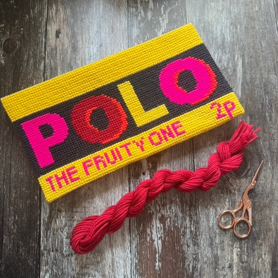 Colorful knitted patch with 'POLO' text on a wooden surface with red yarn and scissors.